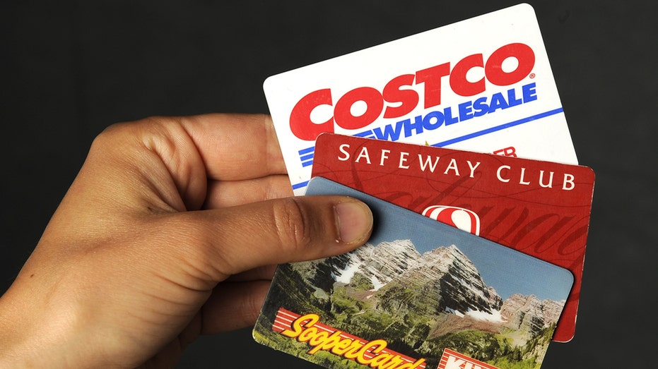 Person holds up a Costco, Safeway and King Soopers cards.